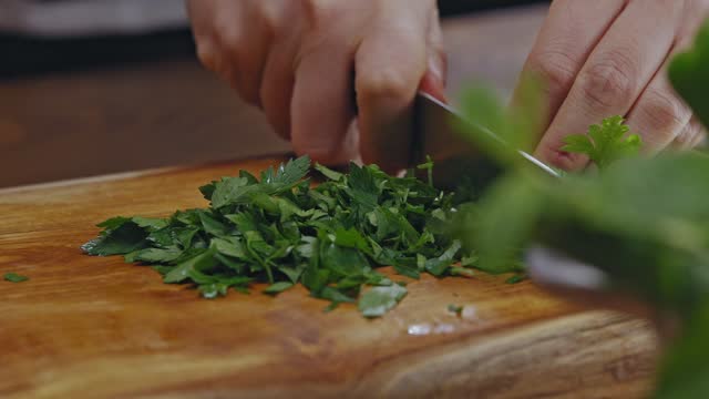 Close-up hands of woman cutting parsley on a wooden floor in the kitchen.