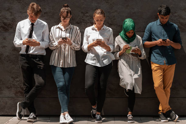 istock Multiethnic group of casual business people using mobile phone during coffee break from work in front of black wall outside 1369537350