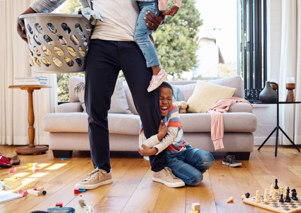 foto de un niño pequeño haciendo una rabieta mientras sostiene la pierna de sus padres en casa - caos fotografías e imágenes de stock