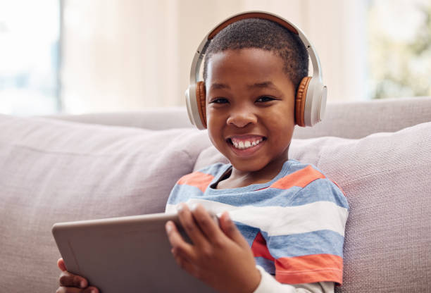 foto de un niño pequeño usando una tableta digital mientras se relaja en casa - happy kid audio fotografías e imágenes de stock