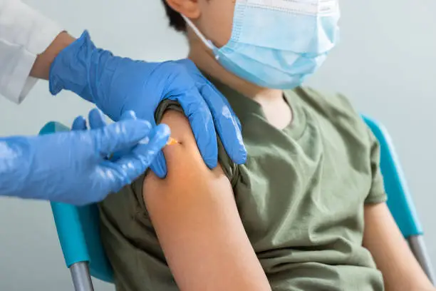 Photo of Close-up of Nurse hands with gloves injecting a vaccine to a young boy.