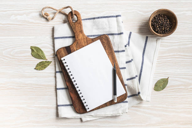 Minimal white kitchen background with blank notebook for text, cutting board, cotton napkin and various spices