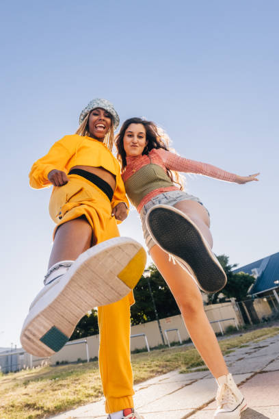 Kicking the air with bestie Kicking the air with bestie. Two female best friends friends having fun while standing together outdoors in the city. Happy female youngsters feeling vibrant and full of life. low angle view stock pictures, royalty-free photos & images