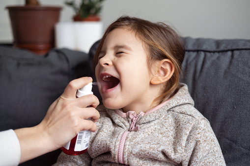 Close up of girl portrait and mother hand with spray for throat. Kids flu medical treatment concept . High quality photo