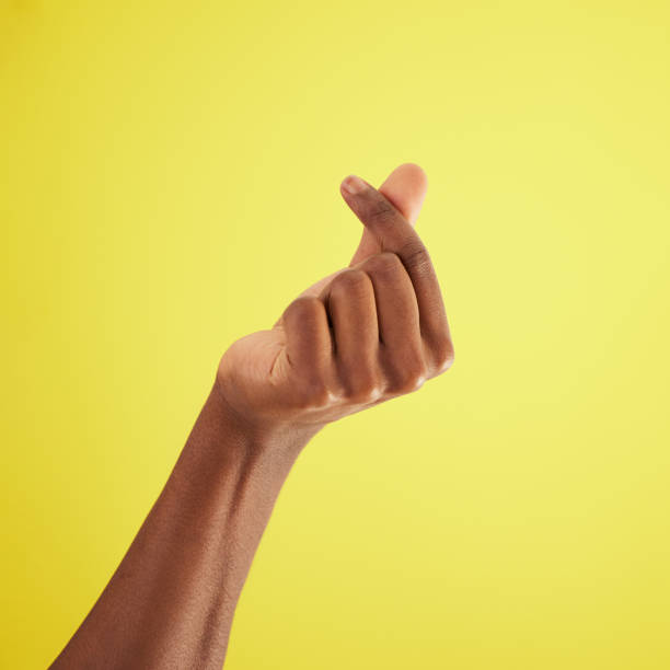 studio shot of an unrecognisable man rubbing his fingers together against a yellow background - snapping imagens e fotografias de stock