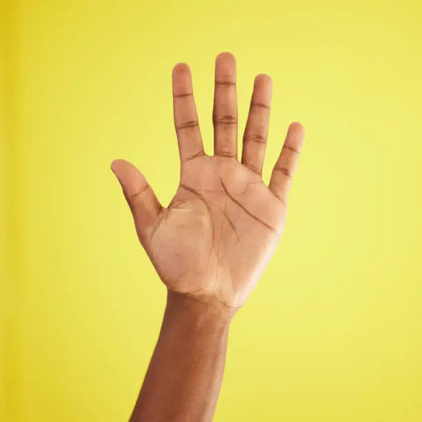 Photo of Studio shot of an unrecognisable man waving against a yellow background