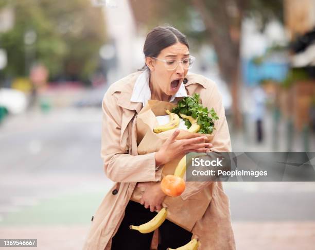 Shot Of A Beautiful Young Woman Trying To Hold Keep Her Groceries From Falling From A Broken Paper Bag Stock Photo - Download Image Now