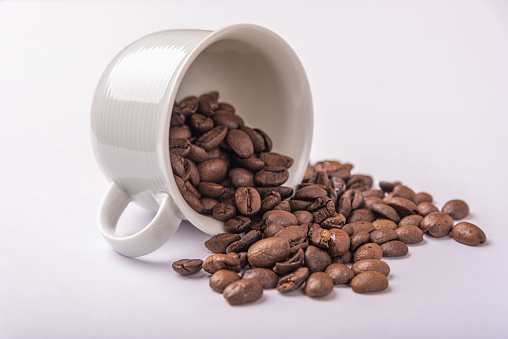 spilled coffee beans white ceramic cup, isolated. High quality photo