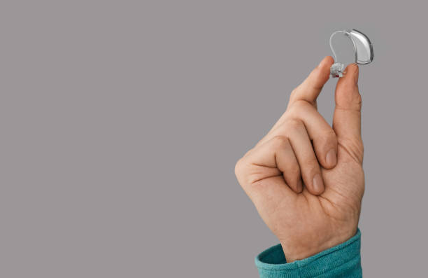 istock Hearing aid in male hand, close-up on gray background with space for text. Hearing solutions, BTE hearing aids 1369553949