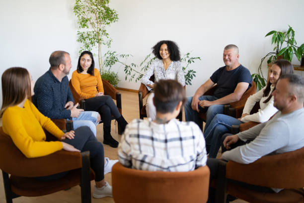 A therapy group having a discussion A group of mixed ethnic people sitting in a circle in comfortable chairs holding a support meeting, as they smile and chat with each other group therapy stock pictures, royalty-free photos & images