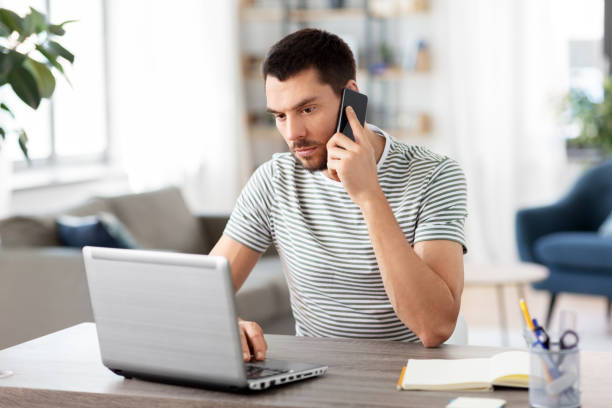 man with laptop calling on phone at home office stock photo