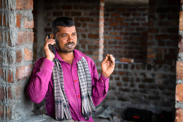 Happy smiling construction labor talking on mobile phone - concept of communication network and technology.