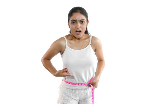 Young woman in casual wear measuring her hip using a measuring tape and indicating weight gain.