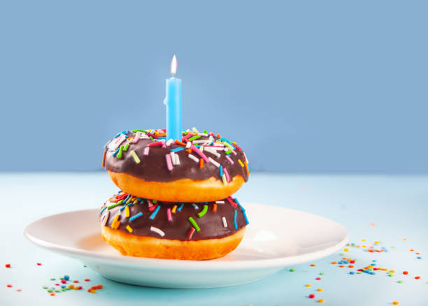 istock Delicious donuts with chocolate icing and birthday candle on the blue background. 1369564623
