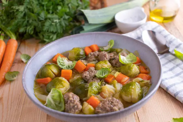 Delicious and healthy low carb stew or soup with vegetables, such as cabbage, brussels sprouts, carrots, onions. Served with meatballs on a deep plate on rustic and wooden table background.