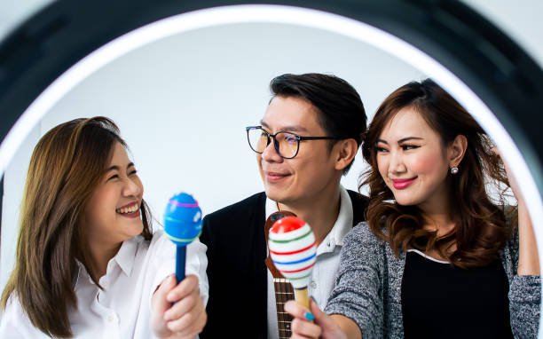 istock Three asian male and female bloggers having fun, playing guitar and dancing while record online video clip. Social Media, Technology and Entertainment Concept. 1369566272