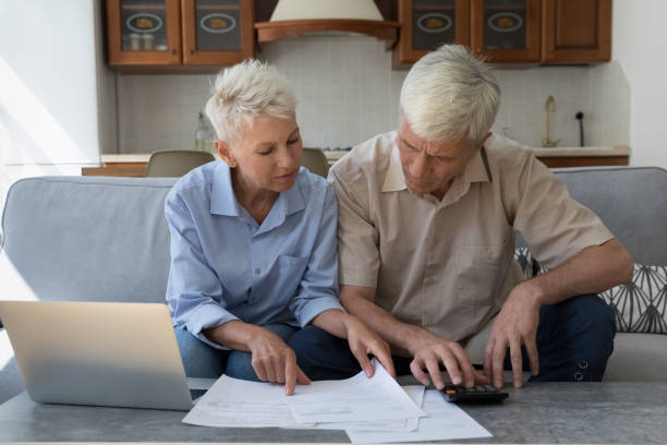 istock Focused older 60s husband and wife paying paper bills 1369567642