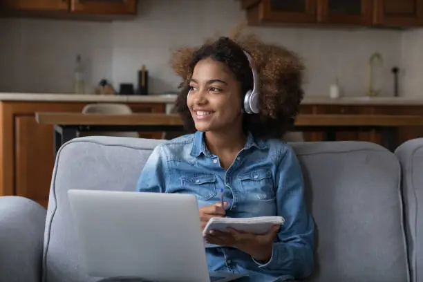 Photo of African teen student girl in wireless headphones studying at home