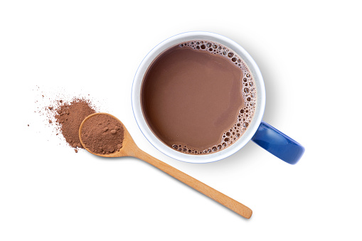 Hot chocolate cocoa drink in blue ceramic mug with cocoa powder in wooden spoon isolated on white background. Top view. Flat lay.