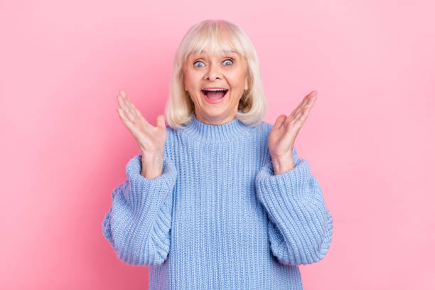 retrato de una atractiva y alegre mujer de cabello gris que aplaude divertirse aislada sobre el fondo de color rosa pastel - mouth open fotos fotografías e imágenes de stock