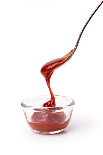 Tomato sauce in spoon pouring into glass bowl isolated on white background with clipping path.