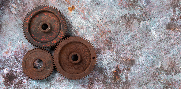 Parts of an old mechanism made of metal gears and other parts covered with rust on a rusty textural background. Technical concept with a copy space, horizontal orientation, top view