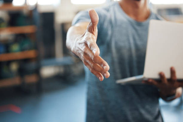 Closeup shot of an unrecognisable man extending a handshake while using a laptop in a gym