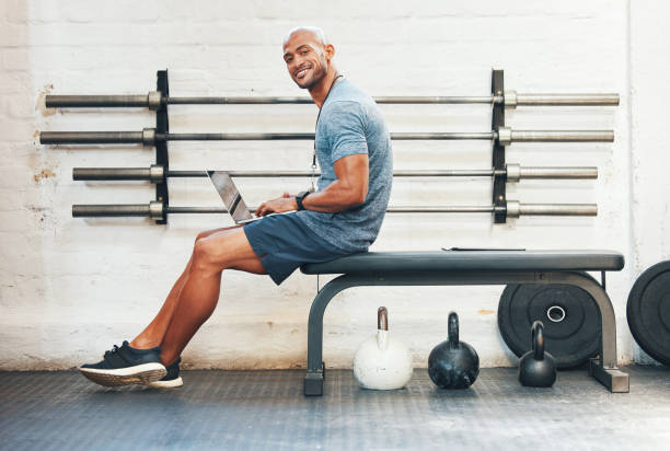 Portrait of a muscular young man using a laptop in a gym I offer online sessions as well gym men africa muscular build stock pictures, royalty-free photos & images