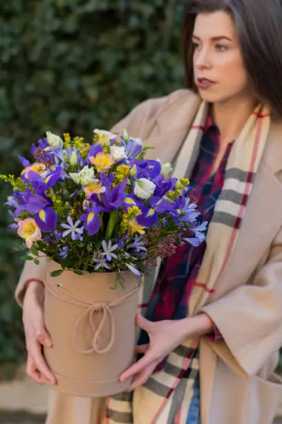 Brunette girl with long hair in her hands a box of spring flowers: irises, eustoma, freesia and others. Concept : flower delivery, birthday gift, Mother's Day bouquet, International Women's Day