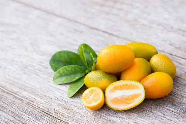 Kumquat or cumquat orange fruit with half sliced and green leaves isolated on white background.