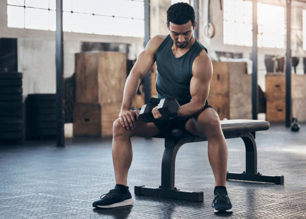 aufnahme eines muskulösen jungen mannes, der mit einer hantel in einem fitnessstudio trainiert - bizeps fotos stock-fotos und bilder