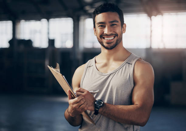 portrait d’un jeune homme musclé écrivant des notes sur un presse-papiers alors qu’il travaillait dans un gymnase - coach exercising instructor gym photos et images de collection