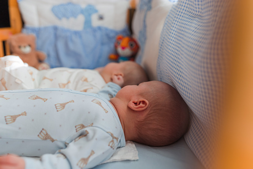 Cute young twin newborn babies taking a nap in a crib