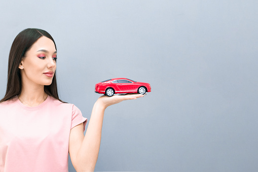 Driving school idea and concept, student driver passed the exam, drivers license, portrait of a beautiful happy young woman, holding a car in her hand. on a gray isolated background. place for text, copyspace