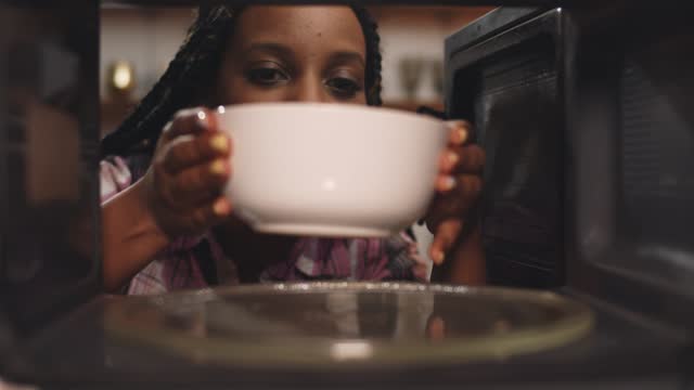African woman reheat food in ceramic bowl using microwave oven