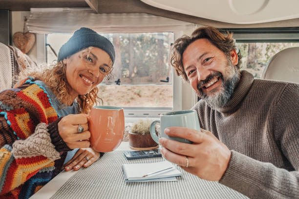 Cheerful adult couple smile and enjoy travel camper van holiday vacation together clinking with cups inside. Happy people tourist posing for a picture indoor. Vanlife lifestyle in the nature stock photo