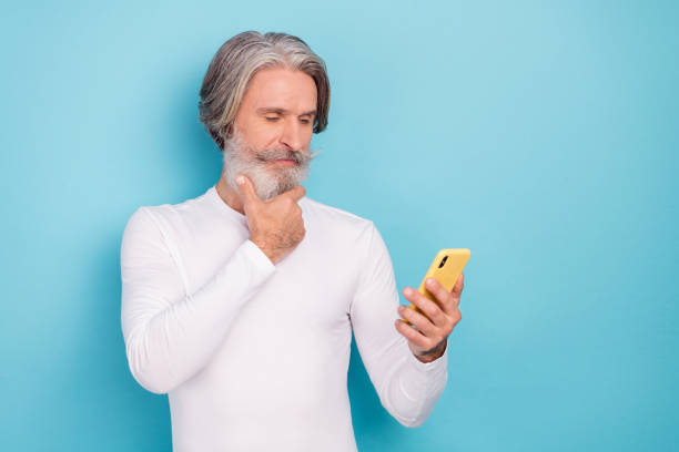 istock Portrait of attractive focused grey-haired man using device thinking reading post smm isolated over bright blue color background 1369578250