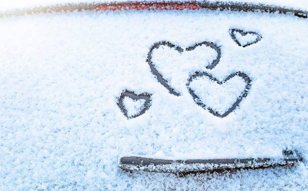 istock Four hearts hand drawing on snow above windshield wiper of car.  Selective focus. 1369578435