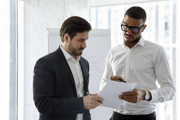 istock Multiethnic millennial coworkers men reading paper together 1369578653