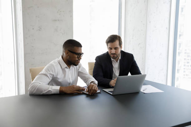 istock Focused diverse businessmen in formalwear using laptop at office table 1369578680