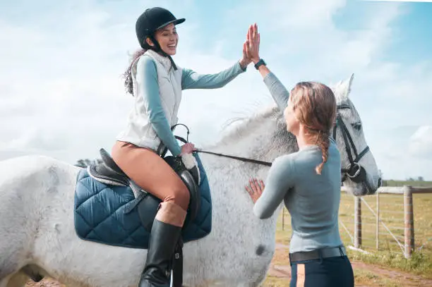 Photo of Shot of an attractive woman and her instructor sharing a high five while out riding in the field