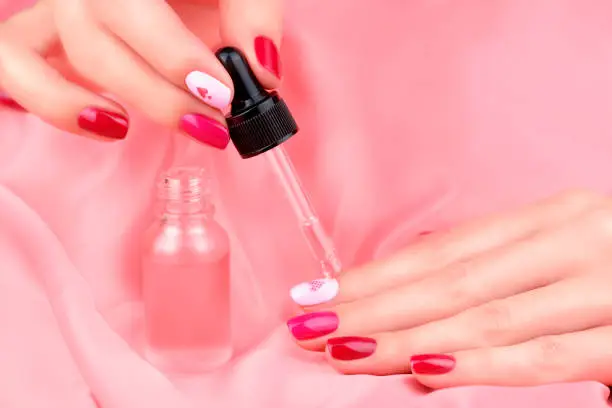 Women's hands with a beautiful manicure in different pink colors. Manicure and cuticle care. A woman's hand drips care oil from a bottle onto her nails. Close up