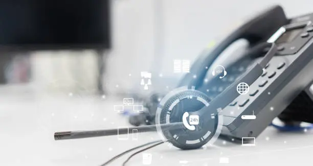 Photo of close up headset of call center and VOIP communication with futuristic virtual icon telecommunication technology on office table in monitoring room for network operation job concept