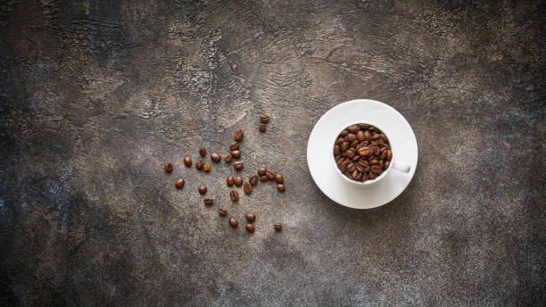 istock Roasted coffee beans in white cup on stone textured background with copy space 1369585849