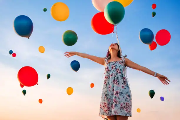 Beautiful young smiling woman and sky full of balloons.