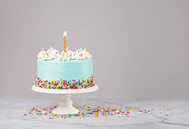 Blue Birthday Cake with sprinkles and Birthday Candle Blue Birthday Cake with colorful sprinkles and lit orange birthday candle over a light grey background. birthday cake stock pictures, royalty-free photos & images