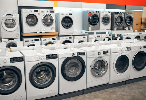 An assortment of beautiful stylish washing machines on showcases in a gadget, electronics and household appliances store.