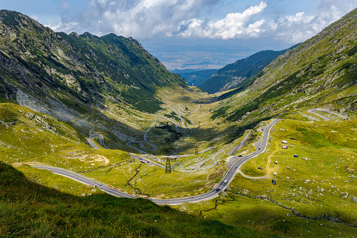 The road curves through a high mountain meadow  towards snowcapped mouuntains
