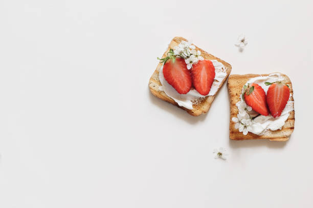istock Two roasted bread sandwiches with cottage cheese and strawberries isolated on white table background. Toasts with fresh fruit and blossoms. Healthy breakfast, morning meal. Flat lay, top view. 1369590062