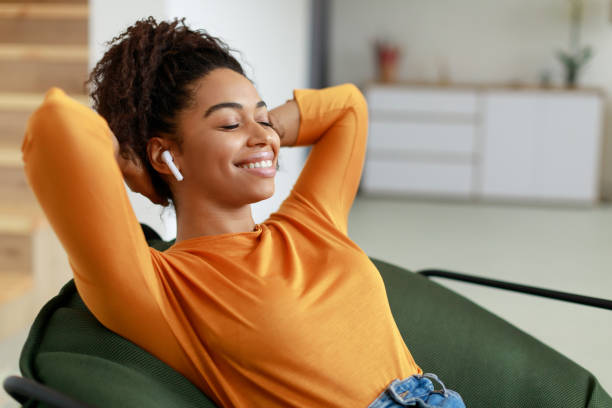 femme noire calme se reposant à la maison sur un sac de haricots - armchair comfortable relaxation headphones photos et images de collection